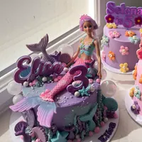 A purple mermaid cake with a doll topper and the name Elisa