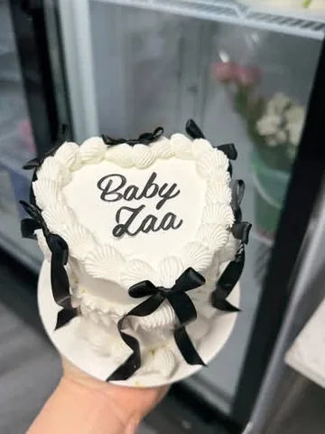 White heart mini cake reading ‘Baby Zaa’ with black bows