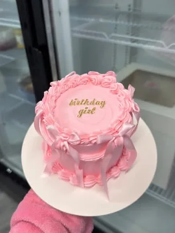 Pink mini cake piped with ‘birthday girl’ in gold, pink ruffles and pink bows