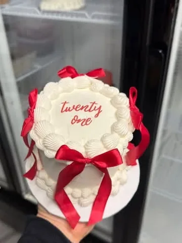 White mini cake reading twenty one in red, with red ribbon bows